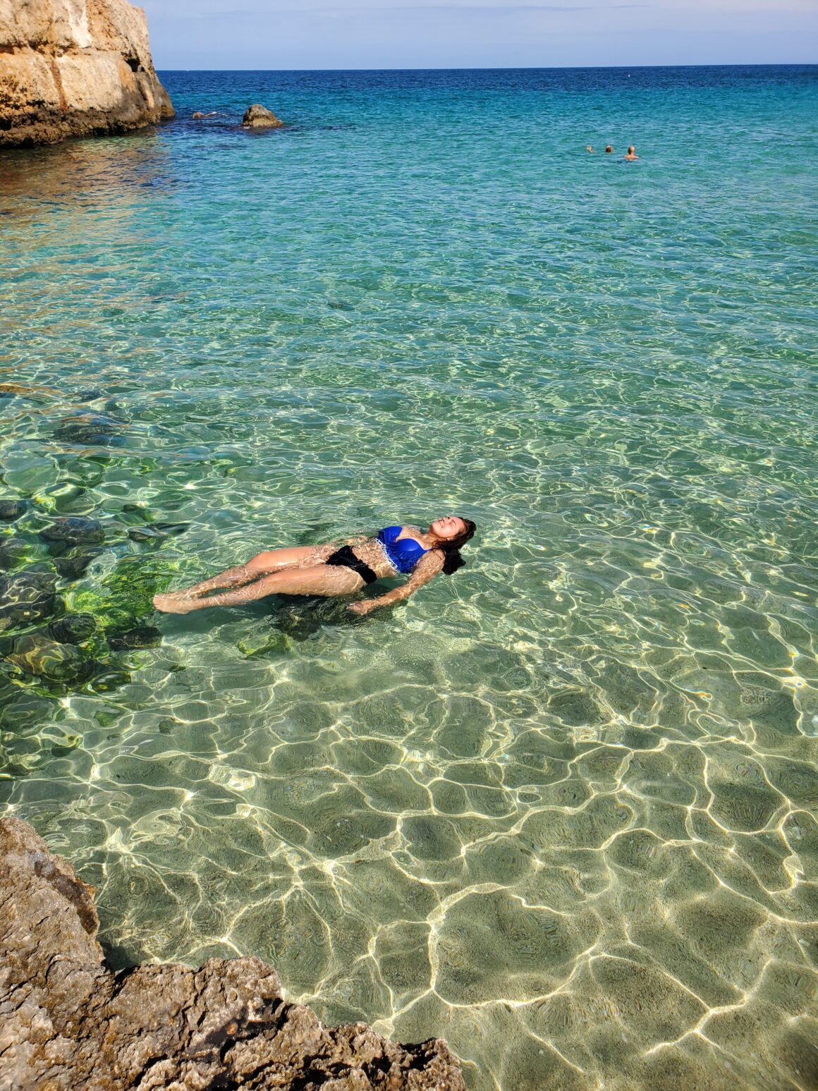 Girl floats in the water at a beach in Monopoli, Italy
