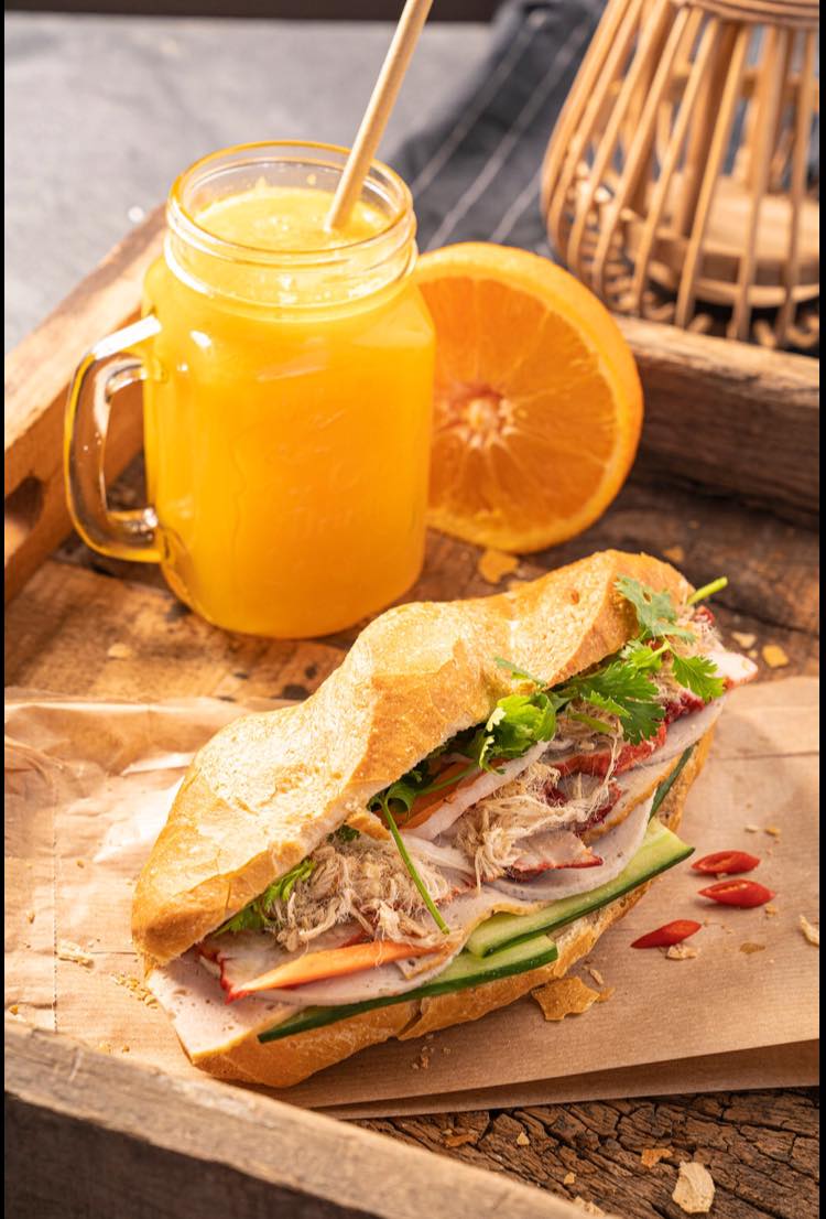 A Bahn Mi next to a glass of orange juice.