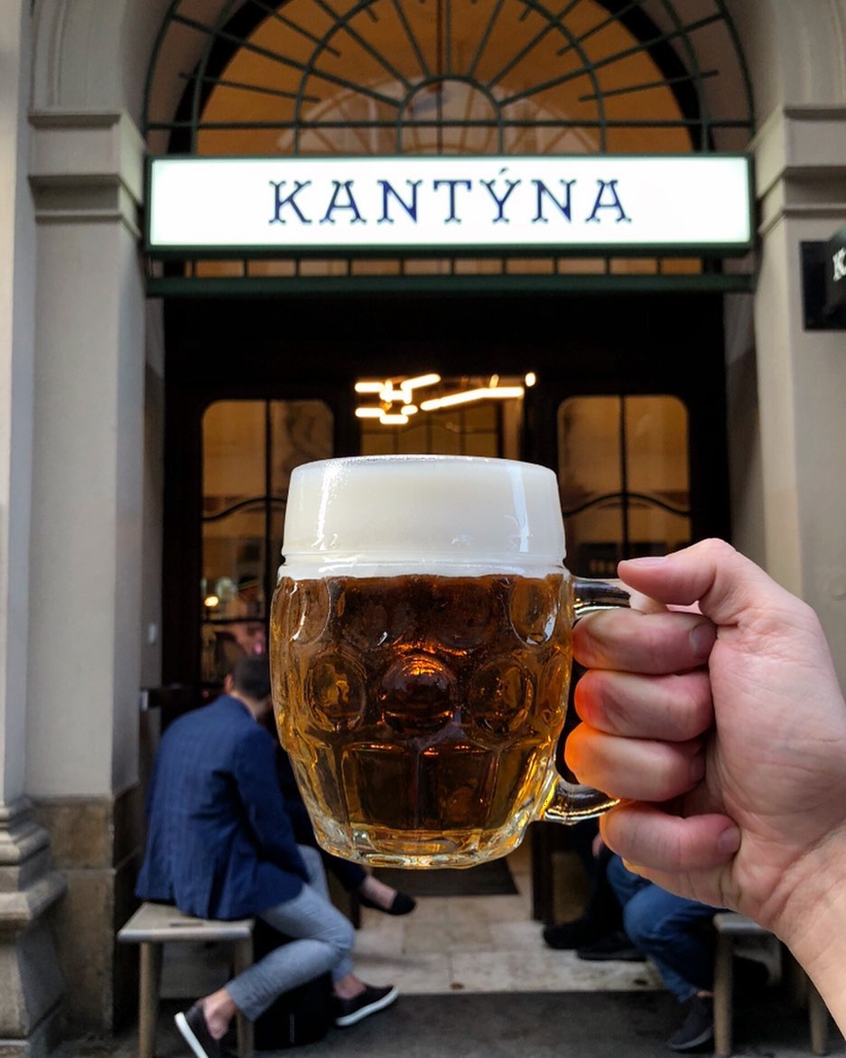 A man holds a beer in front of Kantyna in Prague.