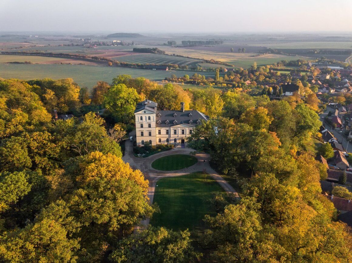 A castle lies in the middle of green fields and orange and yellow trees in the fall, a popular Czech Republic wedding venue
