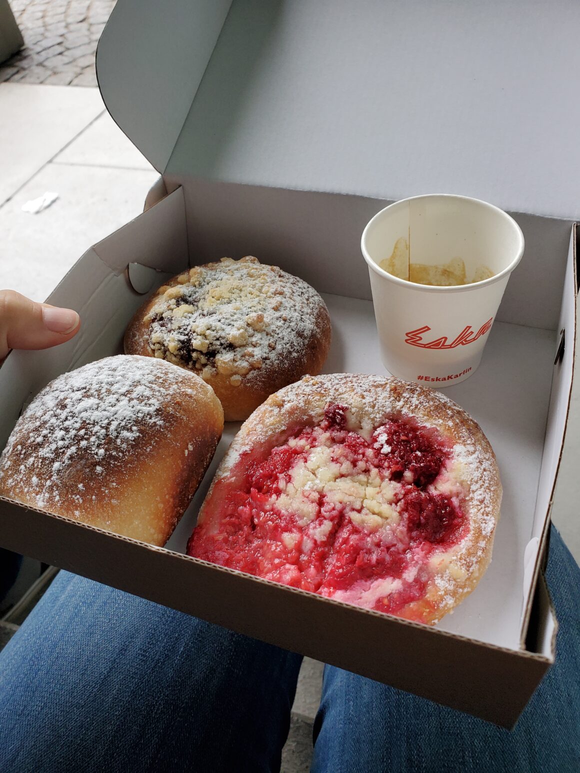 Kolac and buchty, two Czech baked goods featuring fresh fruit in yeasted dough, in a take out box alongside a small cup of espresso.