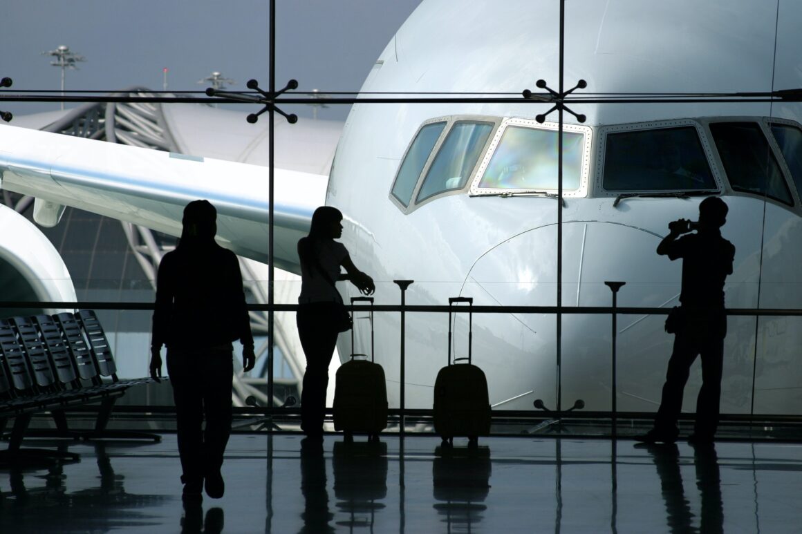 Passengers wait for a flight at an airport with the plane standing behind them