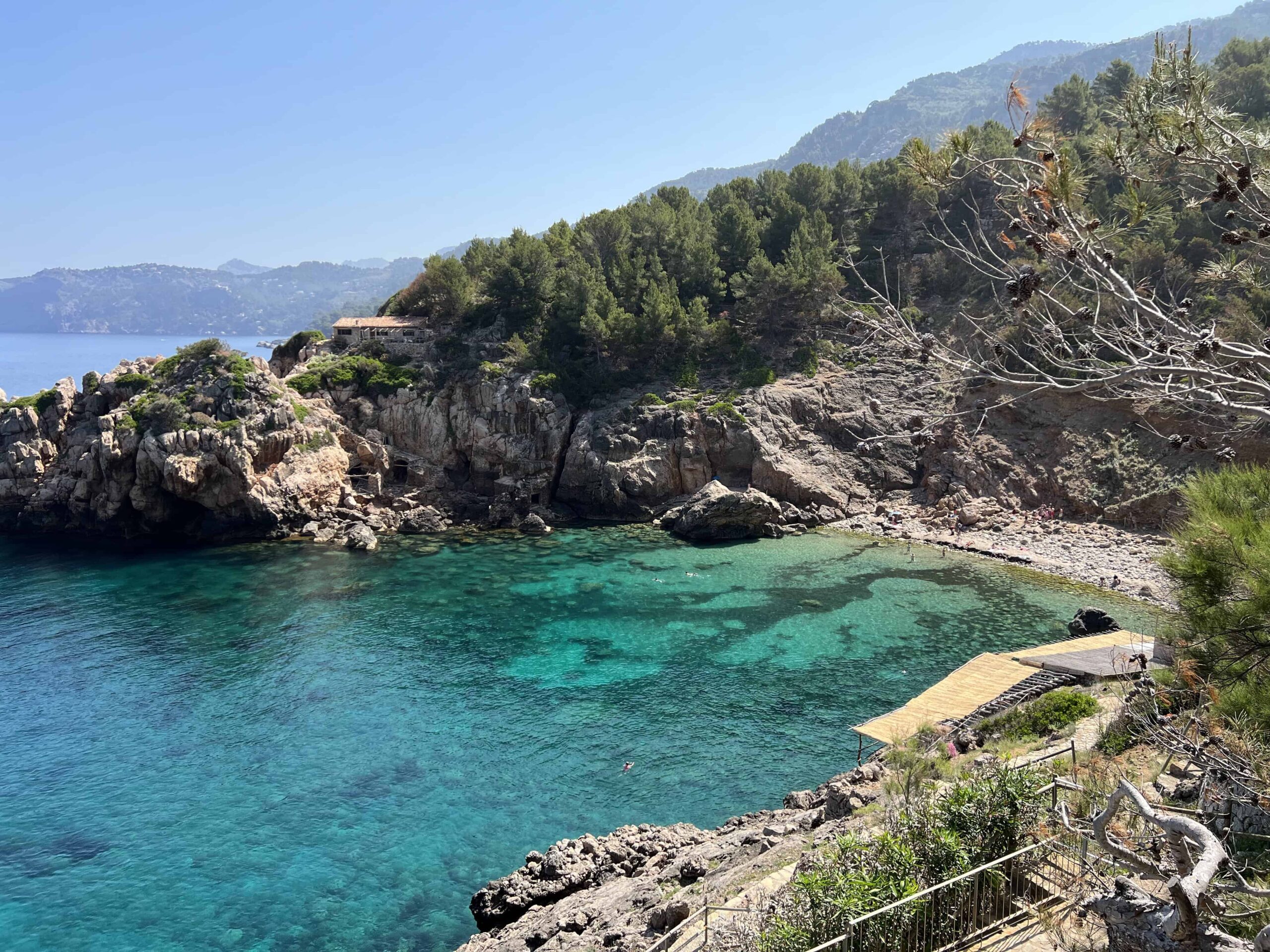 Caia Deia Beach, sunbathers laying on the rocks and swimmers in the water, one of the most beautiful beaches in Mallorca.