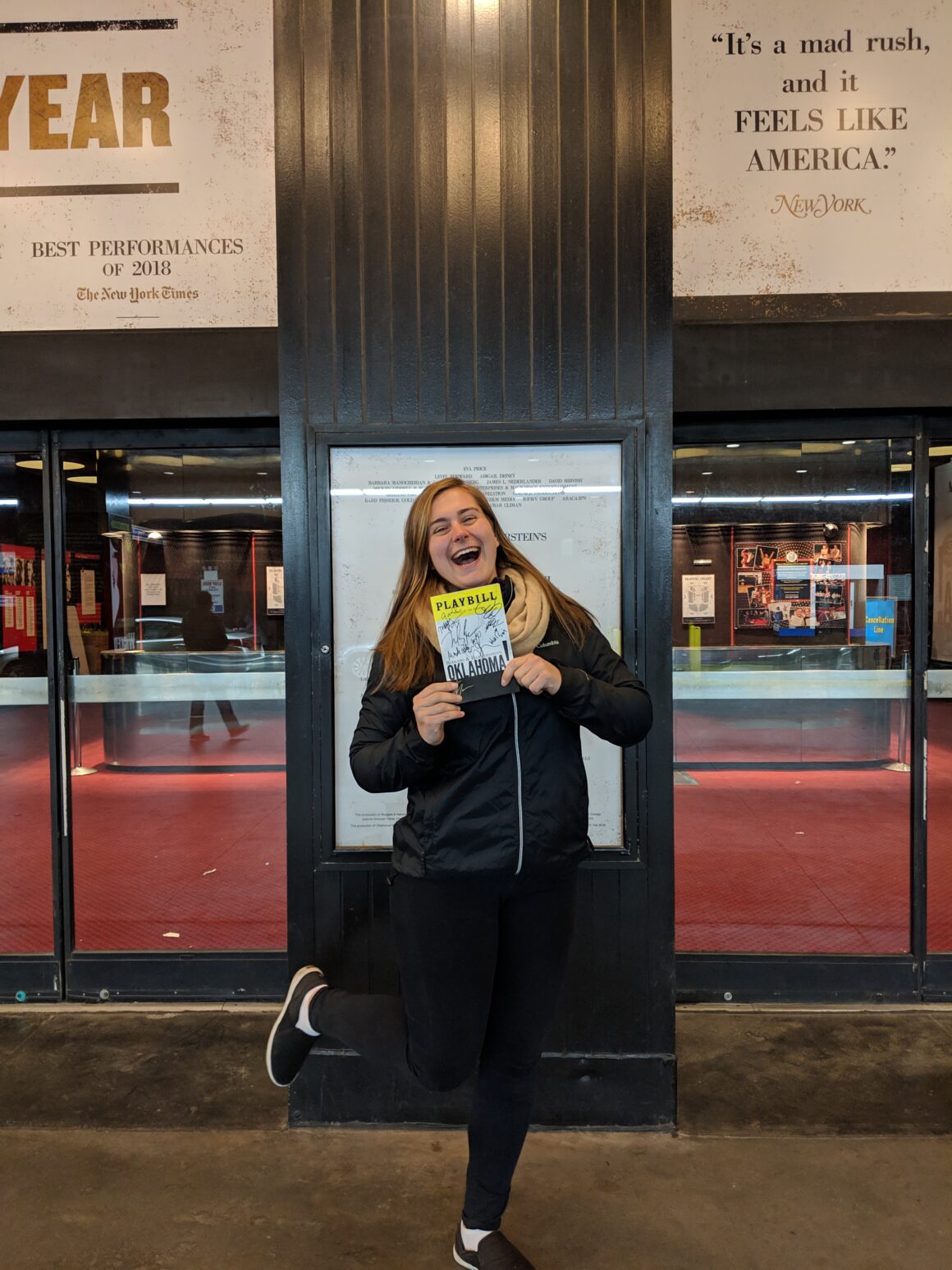 A girl holds a Playbill in front of a Broadway theater