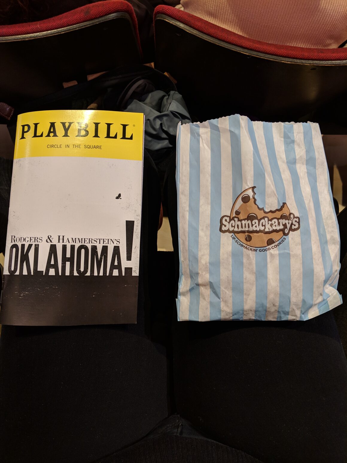 An Oklahoma! playbill sits on a lap next to a stripped bag with cookies