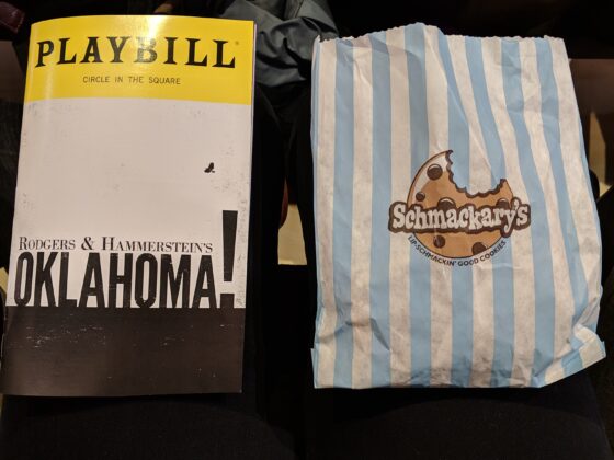 An Oklahoma! playbill sits on a lap next to a stripped bag with cookies