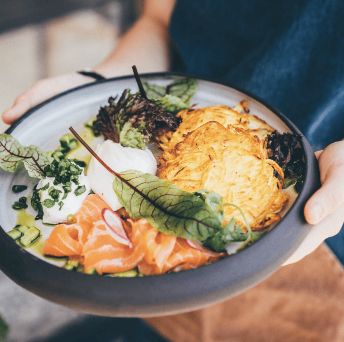 A man holds a bowl of salmon and hashbrowns from NOMADES, one of the best restaurants in Fethiye, Turkey