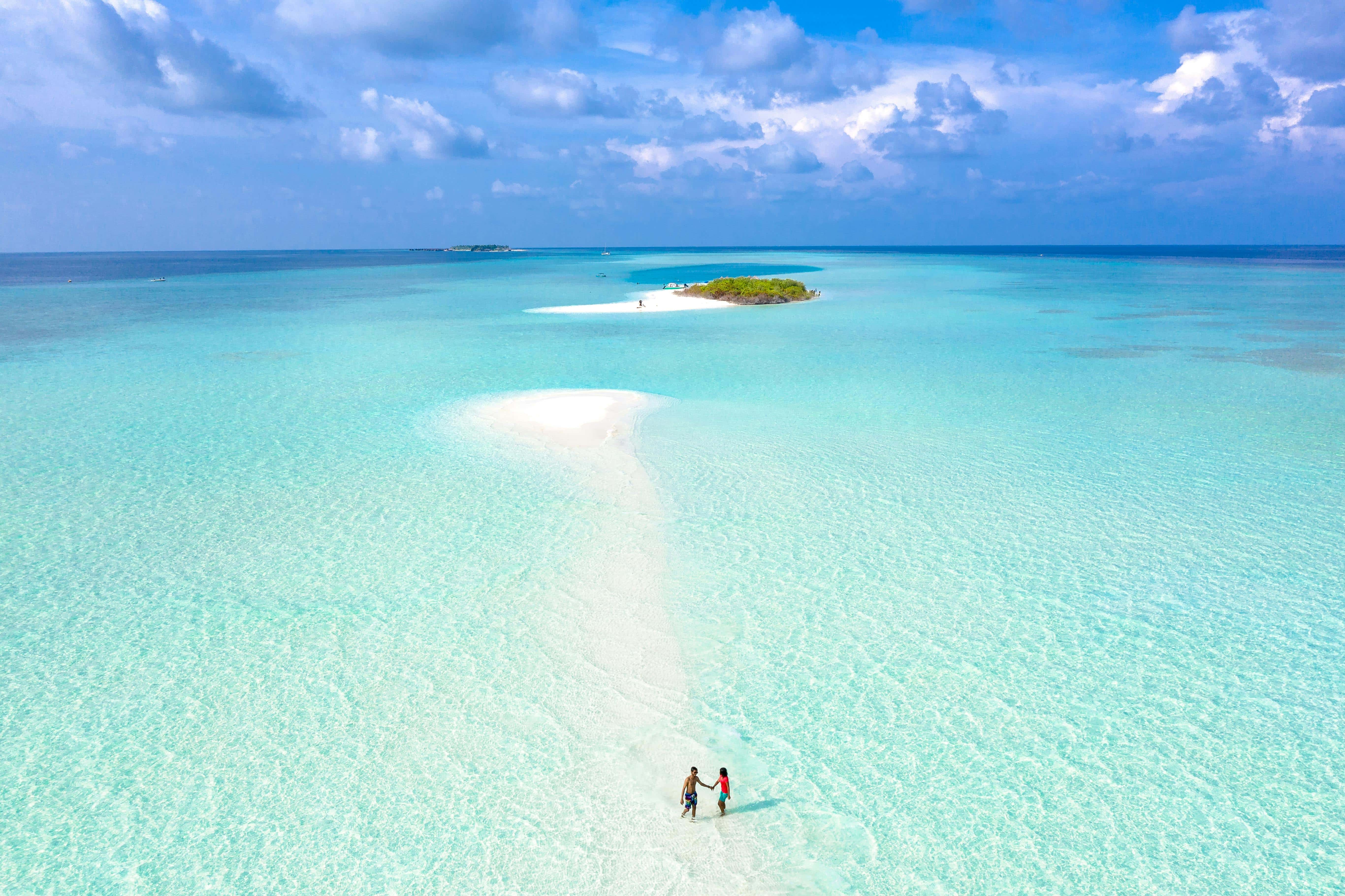 Two people walk on a stretch of sandy beach in the Maldives