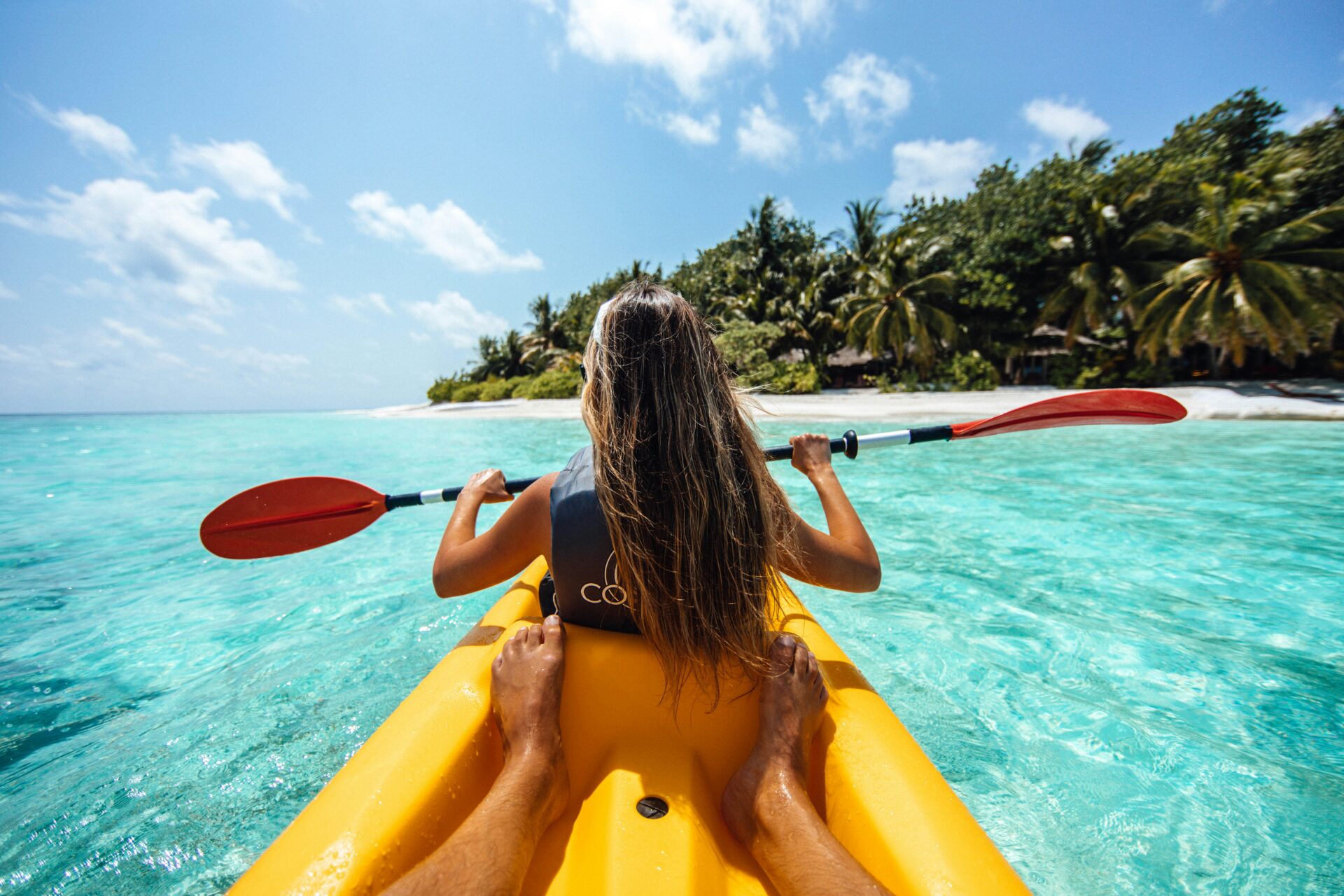 A girl rides a kayak through blue waters in the Maldives during a budget trip to the Maldives