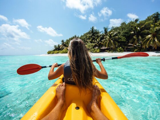 A girl rides a kayak through blue waters in the Maldives during a budget trip to the Maldives